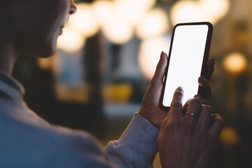 Close up back view of female person holding modern smartphone in darkness and touching with finger...
