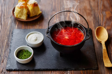 Traditional Ukrainian Russian vegetable borscht on an old wooden background in portioned cast iron. With herbs, sour cream and garlic bread