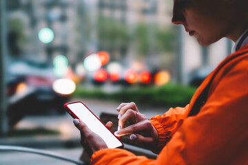 Cropped image of female person in bright orange jacket using modern mobile phone device with touch...
