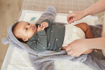 Warm-toned portrait of unrecognizable mother dressing cute mixed-race baby on changing table, copy...