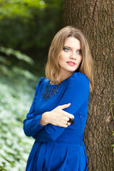 Fototapeta premium Beautiful blonde woman with make up in blue dress in the forest 