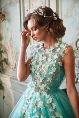 Portrait of a beautiful girl in an airy turquoise dress in the interior.