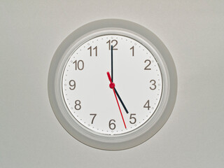 eine Wanduhr auf grauem Hintergrund zeigt die Zeit 05:00 Uhr