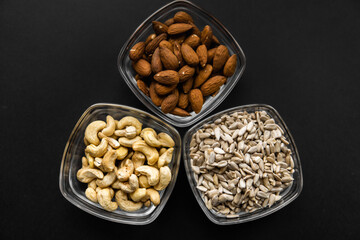 Almond, cashew and sunflower seeds in a small plates which standing on a black table. Nuts is a healthy vegetarian protein and nutritious food.