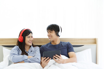 Young Asian Lovely Couple while using Tablet Computer Checking Happy News Watching Movie on bed in Bedroom. Spends time together. White Background. Male and Female.