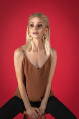 beautiful fashion model with long blond hair sitting on a chair and posing against a red background. hairstyle and makeup are made in a beauty salon