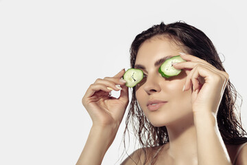 Freshness. Beautiful young woman with cucumber slices near face over white background. Concept of cosmetics, makeup, natural and eco treatment, skin care. Shiny and healthy skin, fashion, healthcare.