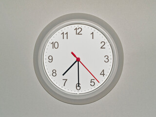 eine Wanduhr auf grauem Hintergrund zeigt die Zeit 07:30 Uhr