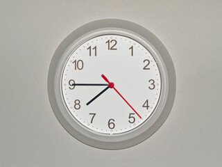 eine Wanduhr auf grauem Hintergrund zeigt die Zeit 07:45 Uhr