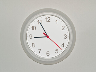 eine Wanduhr auf grauem Hintergrund zeigt die Zeit 08:55 Uhr