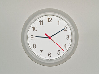 eine Wanduhr auf grauem Hintergrund zeigt die Zeit 09:10 Uhr
