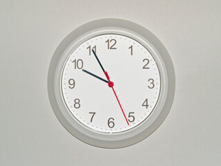 eine Wanduhr auf grauem Hintergrund zeigt die Zeit 09:55 Uhr