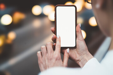 Cropped view of woman's hands holding smartphone and touching with finger on blank display of gadget to install app using internet.Cellular with copy space area for your web page on bokeh background