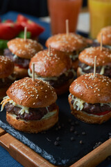 Juicy burgers with onion rings, cucumbers, lettuce, cheese on a black stone background