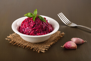 Grated boiled beet salad with garlic and mayonnaise in a white bowl on a brown table. Side dish and...