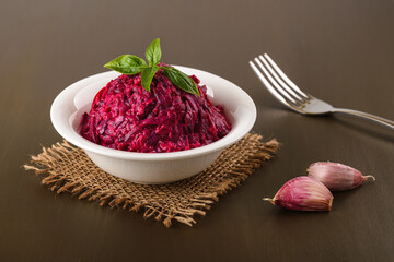 Grated boiled beet salad with garlic and mayonnaise in a white bowl on a brown table. Side dish and vegetarian garnish. Russian cuisine.