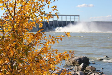 Impressive Hydroelectric dam spillway with water spewing and clouds of spray mist over the river,...
