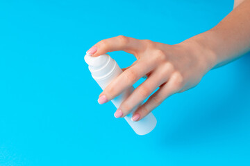 Female hand holding skincare product bottle on blue
