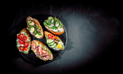Traditional italian bruschetta on toasted slices of baguette seasoned with spice and herbs and garnished with fresh basil on a dark background