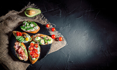 Traditional italian bruschetta on toasted slices of baguette seasoned with spice and herbs and garnished with fresh basil on a dark background
