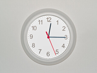 eine Wanduhr auf grauem Hintergrund zeigt die Zeit 12:15 Uhr