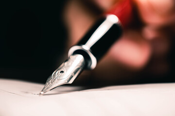 Signing the contract document with fountain pen, close-up shot.