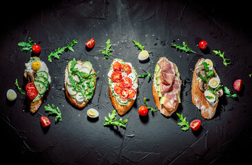 Traditional italian bruschetta on toasted slices of baguette seasoned with spice and herbs and garnished with fresh basil on a dark background