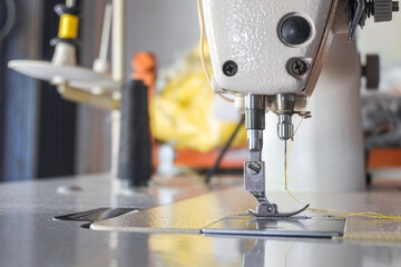 Steel needle presser foot of white industrial sewing machine for sew cloth or fabric with yellow thread roll close-up.