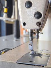 Steel needle presser foot of white industrial sewing machine for sew cloth or fabric with yellow thread roll vertical close-up.