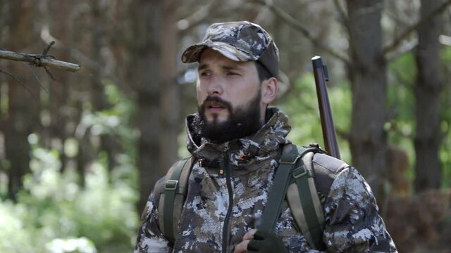 Hunter closes rifle scope and stands in forest and looks around. Outdoor activity concept. Summer hiking in wilderness area. Portrait of man hunter outdoor in forest hunting alone.