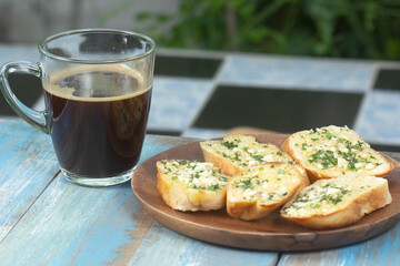 Garlic bread on the wooden plate with black coffee