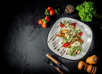 Chicken caesar salad with grilled chicken on plate. Grilled chicken breasts and fresh salad in plate on a dark background. Top view wiht copy space