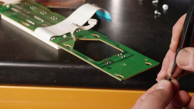 Man's hands fix microswitch of electrical card using tweezers.