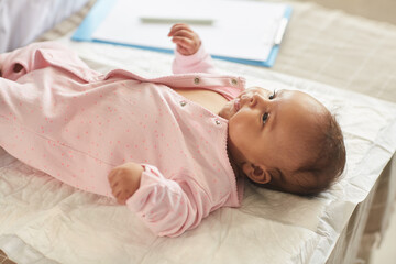 Warm-toned portrait of cute baby girl lying on changing table at doctors office in pink onesie, copy space