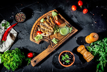 Grilled chicken fillets with herbs and spices served on wooden cutting board on dark background