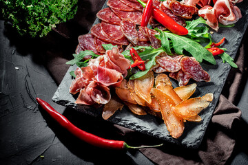 Assorted meat products, including ham, sausage, balyk, lard, basturma, prosciutto on dark background