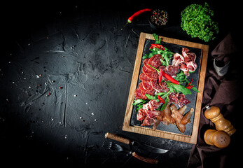 Obraz na płótnie Canvas Assorted meat products, including ham, sausage, balyk, lard, basturma, prosciutto on dark background