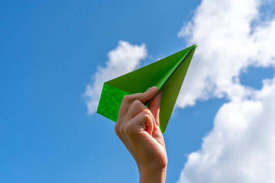 Child hand with paper plane against blue sky