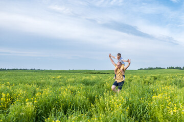 Father and son running and playing on the field at the day time. Concept of friendly family. Great family vacation.