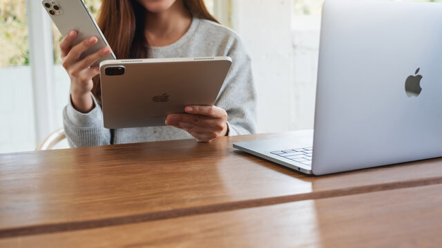 Jun 16th 2020 : An Asian Woman Holding And Using Iphone 11 Pro Max Smart Phone And Apple New Ipad Pro 2020 Tablet Pc With Apple MacBook Pro Laptop Computer On Wooden Table , Chiang Mai Thailand