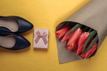 Bouquet of tulips with gift box, heel shoes on a yellow background. Mother's day. Top view. Flat lay
