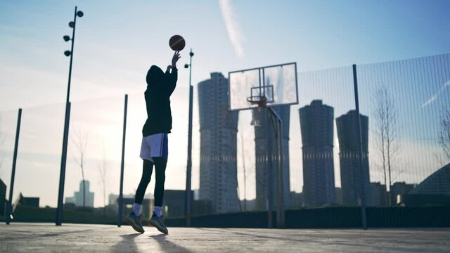 Back view of unrecognizable player throwing ball in a basketball hoop, the ball hits the ring and scores. Slowmotion shot