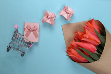 Holiday Shopping. Bouquet of red tulips, gift boxes, supermarket trolley on blue background. Top view