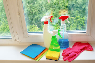 Window cleaning products are located on the windowsill - spray guns, rubber gloves, a sponge and...