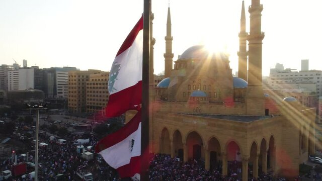 Beirut, Lebanon 2019 : sunset drone shot around Lebanese flag in martyrs square with church and mosque and sun flaring in the background during the Lebanese revolution 