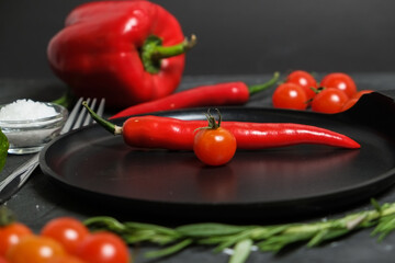 empty round frying pan, fork, fresh rosemary,fresh cherry tomatoes, fresh chilli peppers, garlic, and sea salt on black background.