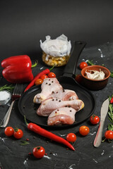 Chicken Leg in a in a frying pan, fresh rosemary, fresh cherry tomatoes, fresh chili peppers, garlic, lime and sea salt on a black background.