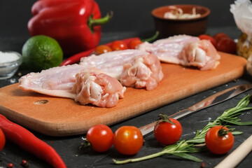 Chicken wings in a wooden Cutting board, fresh rosemary, fresh cherry tomatoes, fresh chili peppers, garlic, lime and sea salt on a black background.