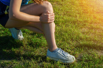 Young woman athlete outdoors sitting on grass touching painful twisted ankle. Running leg injury accident woman runners. Ankle sprain pain.