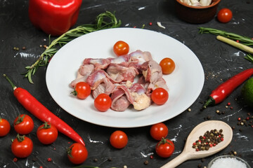 Chicken ventricles in a in a white plate, fresh rosemary, fresh cherry tomatoes, fresh chili peppers, garlic, lime and sea salt on a black background.